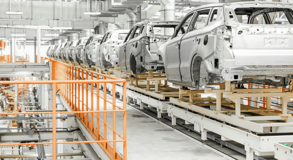 Caisses en blanc sur skids transportées par un convoyeur à rouleaux dans un atelier de ferrage automobile